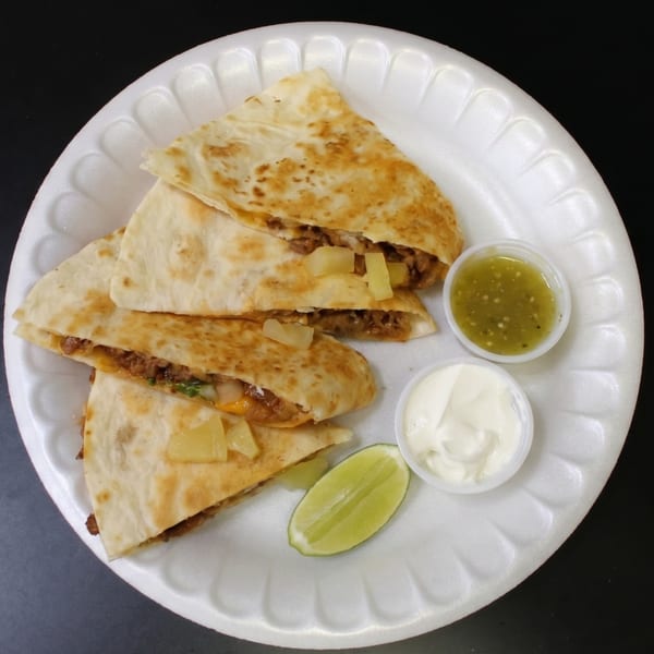 Four quesadilla slices with meat, cheese, and pineapple, served with salsa verde, sour cream, and lime.