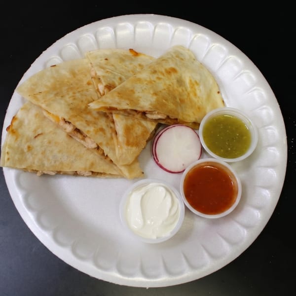 Chicken quesadillas on a white plate with green salsa, red salsa, sour cream, and radish slices.
