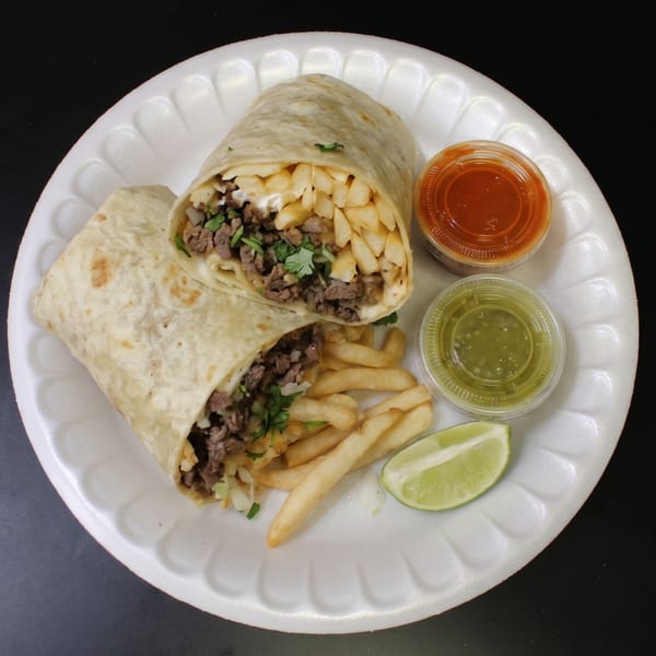 Two halves of a carne asada burrito with fries, red and green salsa, and a lime wedge.