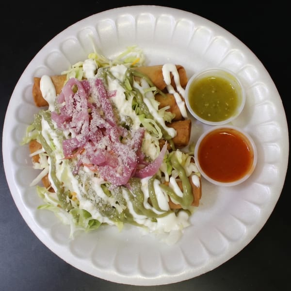 Four taquitos topped with cabbage, pickled onions, cheese, and sauces, with two dipping sauces.