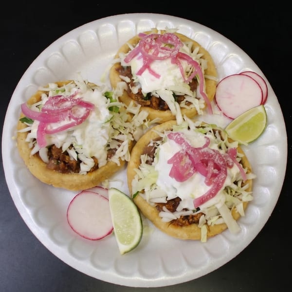Three sopes with meat, cabbage, sour cream, pickled red onions, radishes, and lime wedges.