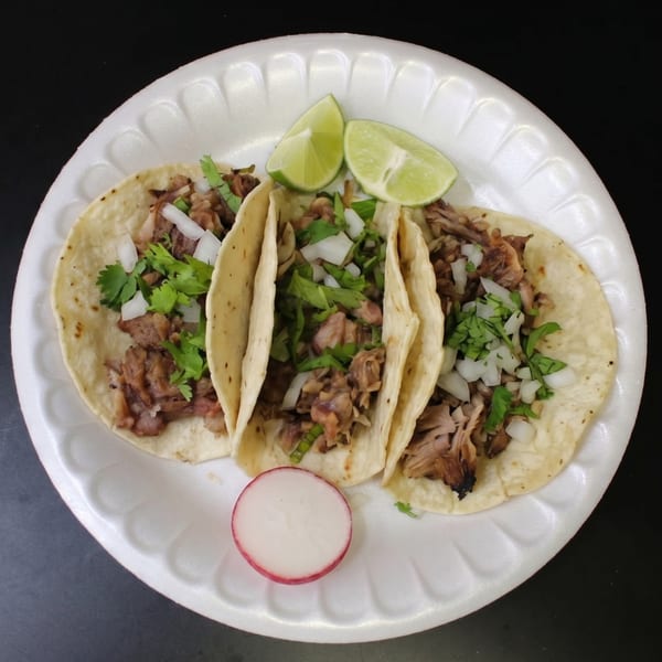 Three street tacos with meat, cilantro, and onions, served with lime wedges and a radish slice.