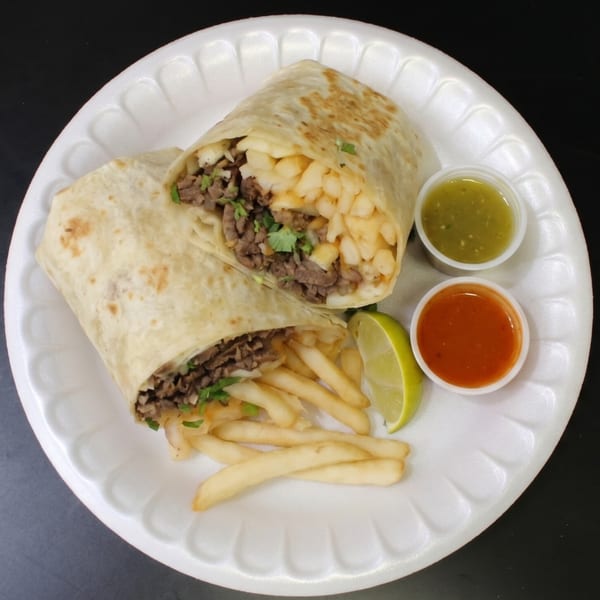 Two burritos filled with meat and fries, served with a side of fries, lime, and two sauces.