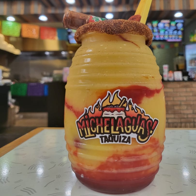 A large Michelaguas! Taquiza mango drink with chili powder rim and a small hot sauce bottle.